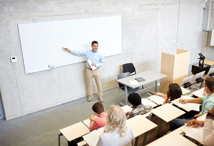 一张教室的照片，老师指着黑板，学生们在听。